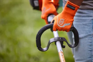 A person holding a Husqvarna product with visible gloves, focusing on the handle grip.