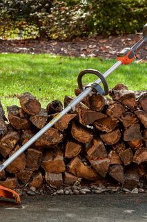 A string trimmer and battery charger placed on a stack of cut tree logs in a garden setting.