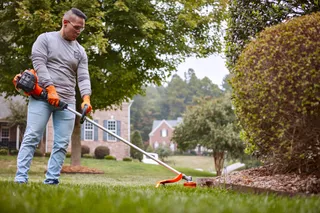 A person using a string trimmer to edge a lawn in a residential garden.