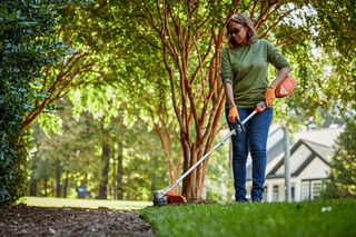 A person using a string trimmer to edge a lawn in a garden setting.