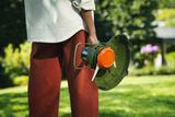 Person holding a grass trimmer, close-up of trimmer head and guard in a garden.