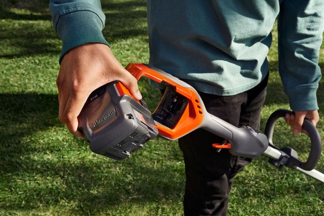 Una persona che tiene in mano un prodotto Husqvarna e mostra il vano batteria.