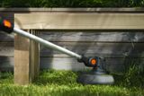 Close-up of a grass trimmer cutting lawn edges beneath a wooden garden bench.