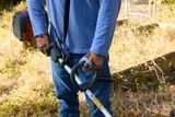 A person holding a Husqvarna grass trimmer in a garden setting.