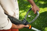 Close-up of hands adjusting the rotating auxiliary handle on a grass trimmer in a garden.
