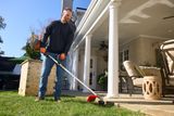A person using a string trimmer to edge a lawn near a patio area.