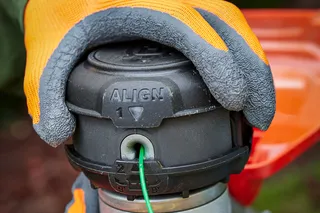 Close-up of a person wearing gloves, assembling a trimmer head with visible alignment markings.