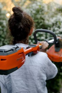 一个人拿着 Husqvarna 富世华割灌机穿过鲜花盛开的花园。