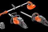 Top view of various Husqvarna battery-powered gardening tools including a hedge trimmer, chainsaw, and grass trimmer.