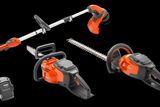 Studio image of Husqvarna gardening tools including a chainsaw, hedge trimmer, and grass trimmer, with batteries.