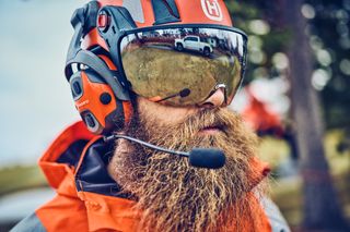 Osoba ubrana w sprzęt roboczy i kask ochronny Husqvarna z wizjerem i ochronnikami słuchu.