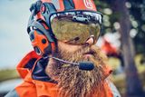 Une personne portant des équipements de travail et un casque de sécurité Husqvarna avec visière et protège-oreilles.