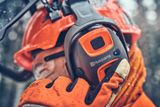 Nahaufnahme einer Person, die Husqvarna-Arbeitskleidung trägt und den Gehörschutz mit einem sichtbaren Logo in den Mittelpunkt stellt.
