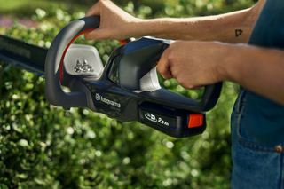 Uma pessoa a aparar sebes com um corta-sebes Husqvarna num jardim.