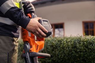 Eine Person, die ein Husqvarna-Gerät in der Hand hält und das Batteriefach zeigt.