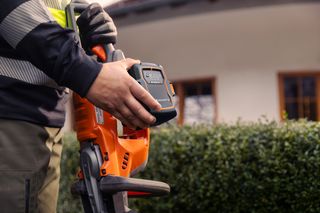 Una persona che tiene in mano un prodotto Husqvarna e mostra il vano batteria.