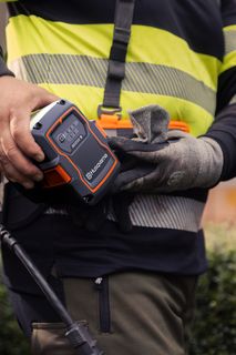 Osoba vkladajúca batériu do produktu v záhradnom prostredí.