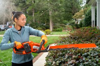 A person using a hedge trimmer to trim bushes in a garden.