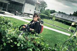 A person trimming a hedge with a hedge trimmer in a garden setting.