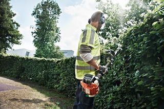 A person trimming a hedge with a power tool in a garden setting.
