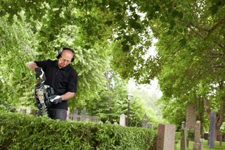 A person trimming a hedge with a power tool in a garden setting.