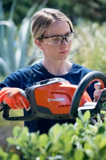 Osoba używająca nożyc do żywopłotu do przycinania krzewów w ogrodzie.