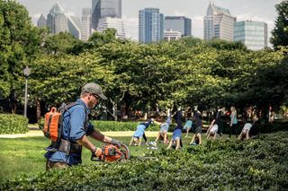 街のスカイラインを背景にした公園でヘッジトリマーを使っている人。
