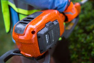Close-up of a person holding a Husqvarna hedge trimmer, showcasing the battery compartment.
