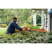 Une personne qui taille des haies avec une scie à chaîne dans un jardin résidentiel.