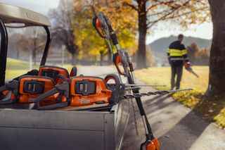 A collection of hedge trimmers and chainsaws on a vehicle, with a person using a leaf blower in a park.