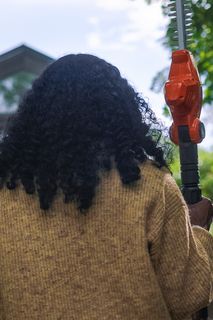 A person holding a hedge trimmer, facing away, in a garden setting.