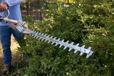Une personne taillant des buissons avec un taille-haie Husqvarna dans un jardin.