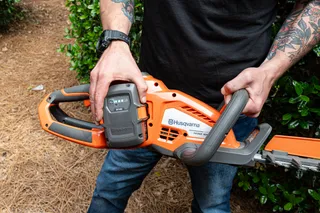 A person holding a Husqvarna hedge trimmer, showcasing the battery compartment.