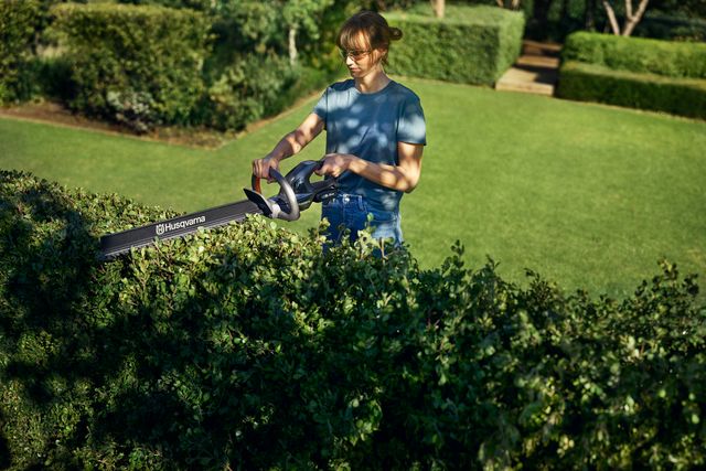 En person som klipper en häck i en trädgård med en Husqvarna-häcksax.