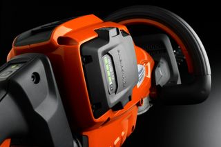 Close-up of a Husqvarna chainsaw handle and battery compartment.