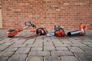Un ensemble d’outils de jardinage Husqvarna, y compris une tondeuse, une scie à chaîne et un souffleur de feuilles sur une surface pavée.