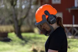 Persoon die buiten een boswerkhelm met gaasgelaatsscherm draagt in de buurt van een rood gebouw.