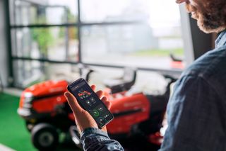 A person using a smartphone app to control a ride-on mower in a showroom.