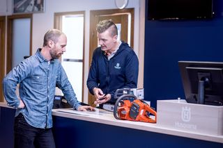 Two people at a counter discussing a Husqvarna chainsaw.