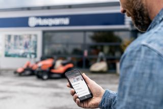 Eine Person mit einem Smartphone mit Husqvarna Connect-App im Hintergrund.