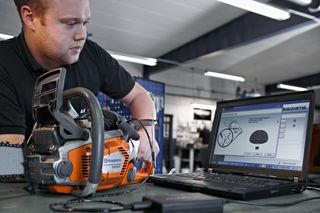 Dirbtuvių aplinkoje dirbantis asmuo, naudojantis nešiojamąjį kompiuterį Husqvarna grandininio pjūklo nustatymams reguliuoti.