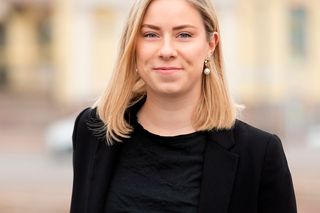 Henkilö keskikokoisessa muotokuvassa ulkona, taustalla sumennetut kaupunkirakennukset.