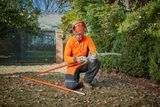 A person in work gear assembling a pole saw in a garden setting.