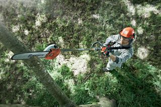 A person using a pole saw to trim tree branches from an elevated position.