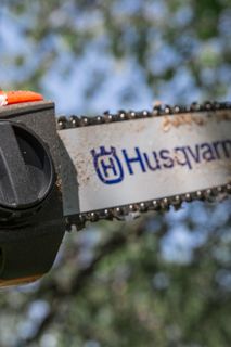 Close-up of a Husqvarna chainsaw blade and tension adjustment knob.