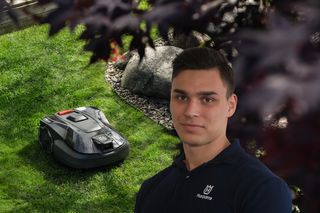 Ein Mähroboter auf einer Wiese mit einem modernen Unterhaus im Hintergrund.