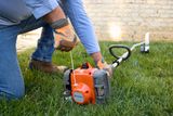 A person starting a Husqvarna grass trimmer on a lawn.