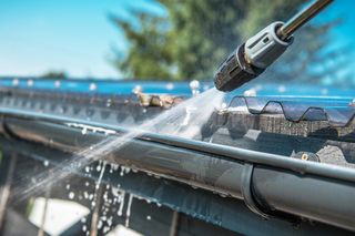 A pressure washer cleaning a metal roof gutter.