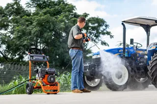 A person using a pressure washer to clean a tractor outdoors.