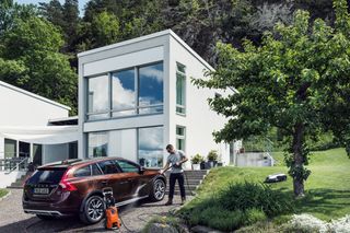 A person washing a car with a pressure washer in a residential garden setting.